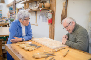 mentor carves wood while apprentice watches