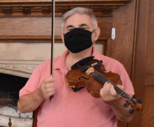man in pink shirt holding fiddle and smiling behind a mask